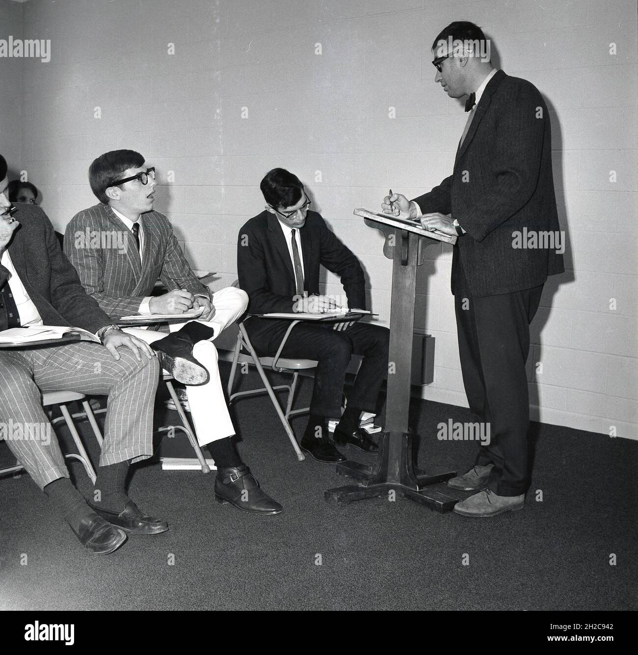 1960s, historical, in a room some male undergraduate students sitting on metal chairs listening to a teacher standing at a lectern, giving a talk in a philosophy class, Monroe College, USA Stock Photo