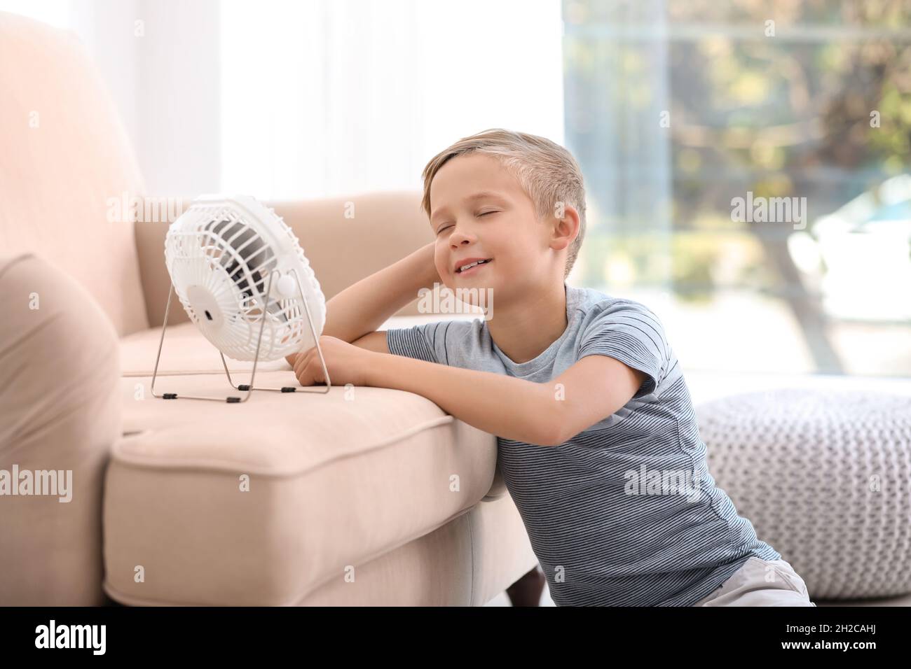 Little boy relaxing in front of fan at home. Summer heat Stock Photo