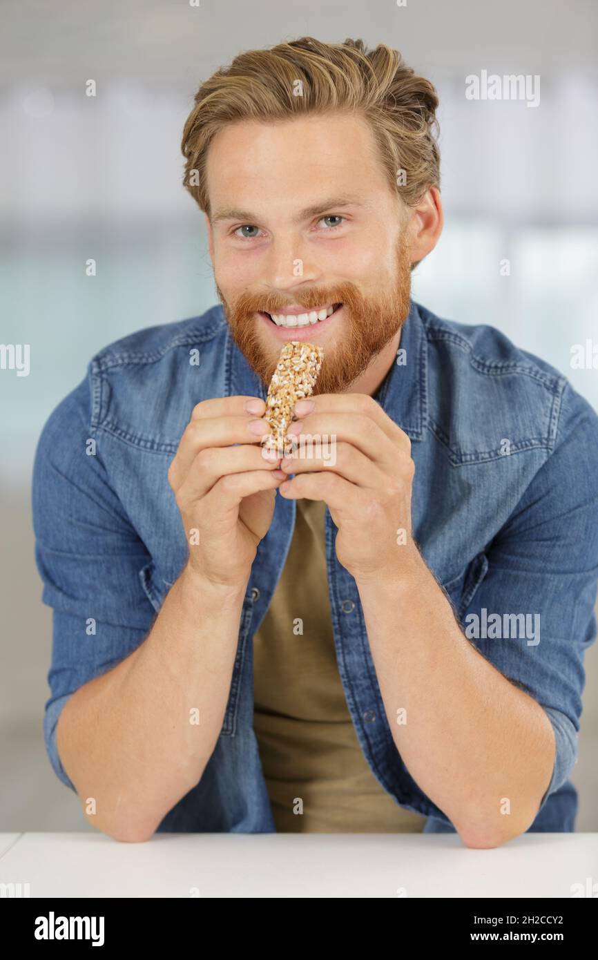 man eating an unwrapped cereal bar at home Stock Photo