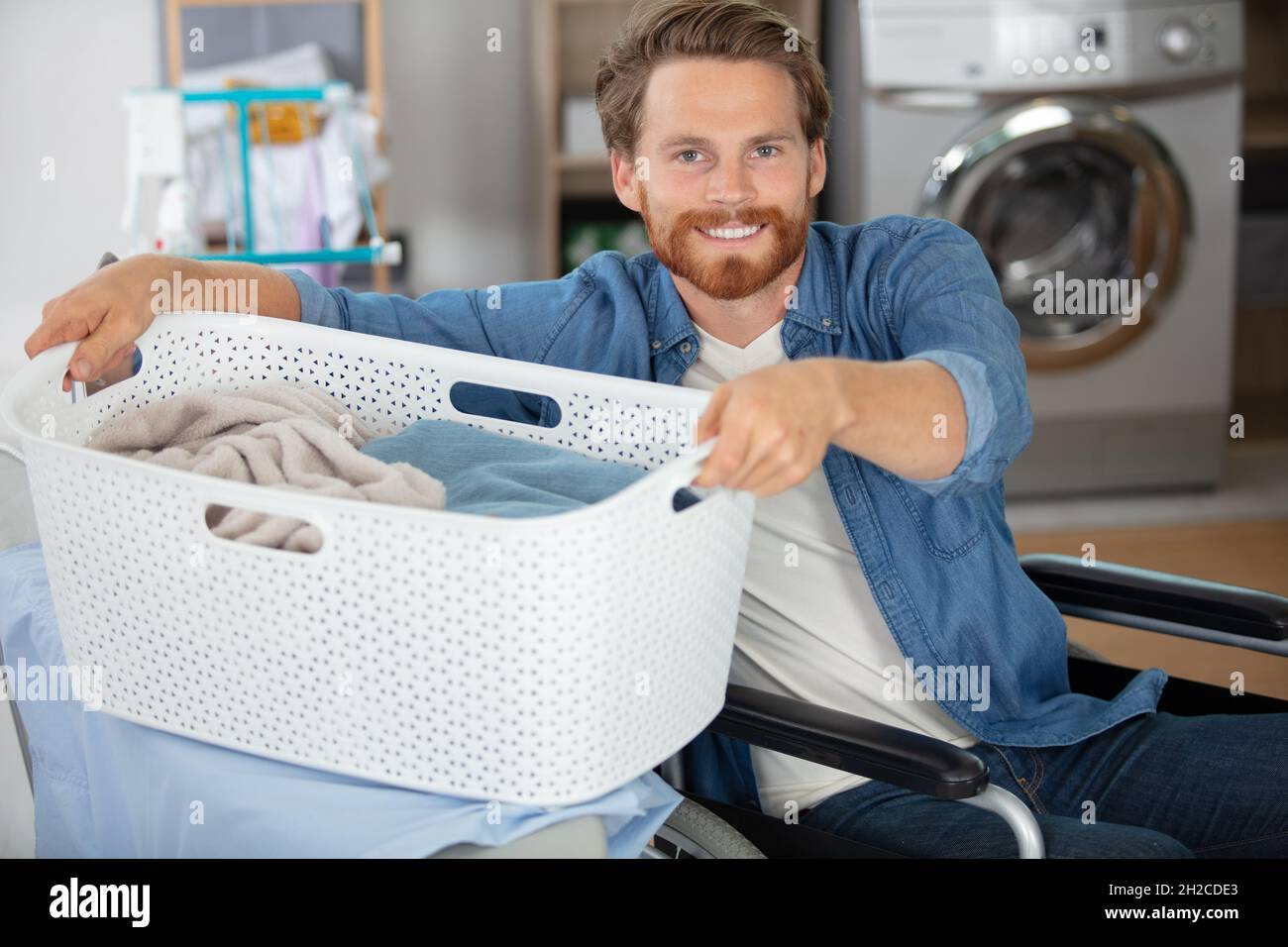man in wheelchair lifting laundry basket on to ironing board Stock