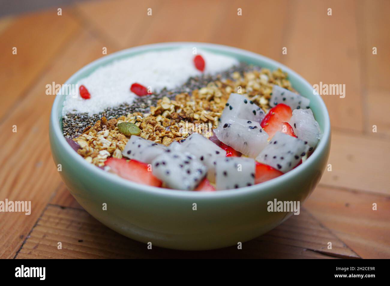 Granola yoghurt bowl with cereal strawberry pitaya fruits coconut flake and lycium chinense on wooden table Stock Photo