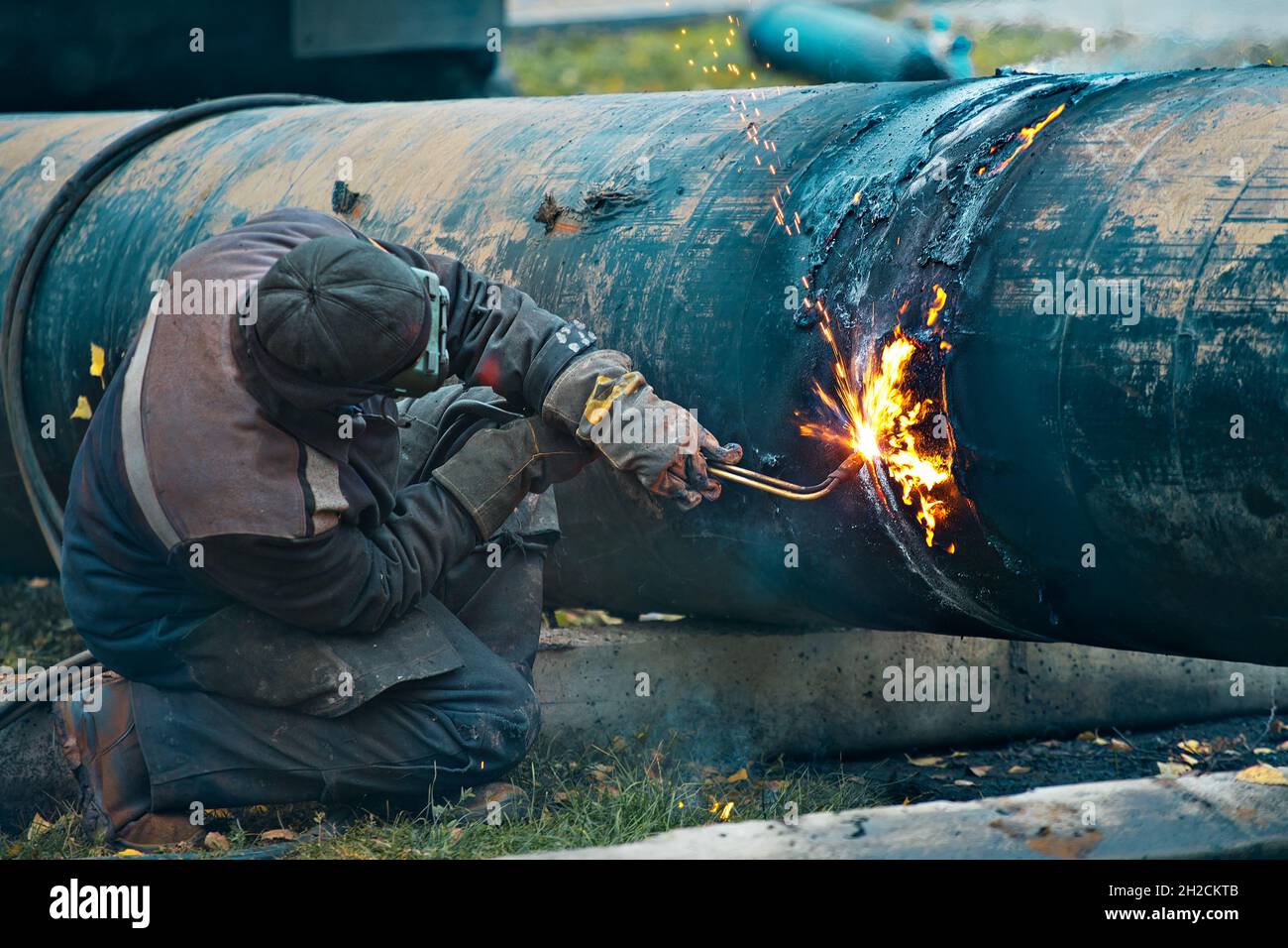 The welder cuts large metal pipes with ocetylene welding. A worker on