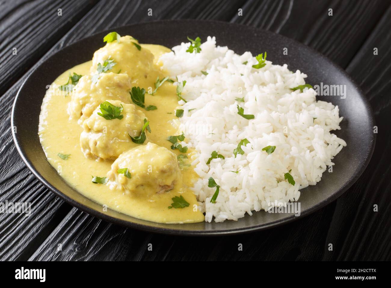 Traditional recipe for Danish Meatballs in Curry Boller i Karry with rice garnish close up in the plate on the table. horizontal Stock Photo