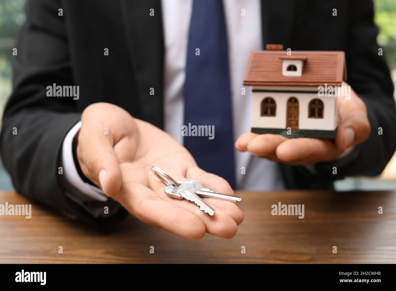 Real estate agent holding house model and keys at table Stock Photo - Alamy