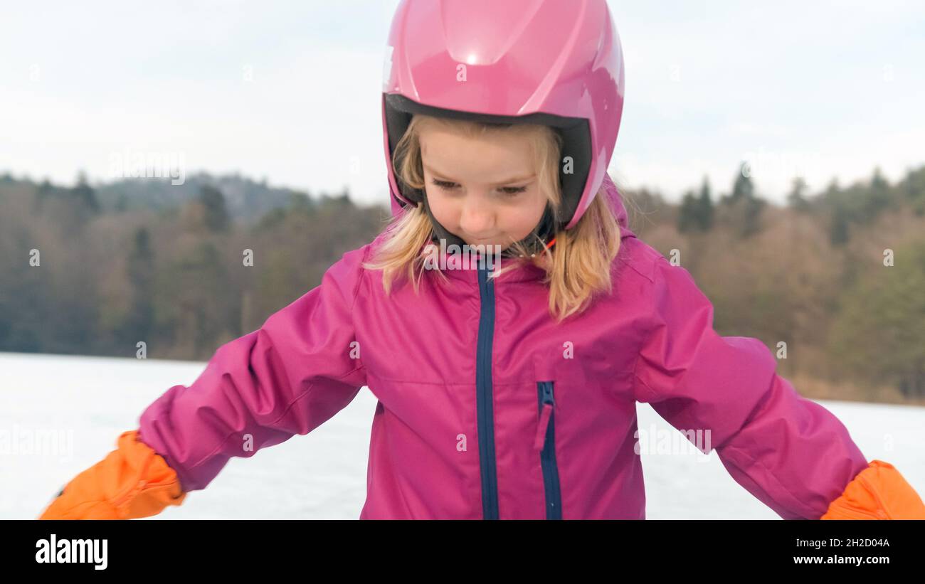Cute little girl, wearing a snowsuit and helmet, trying to stand