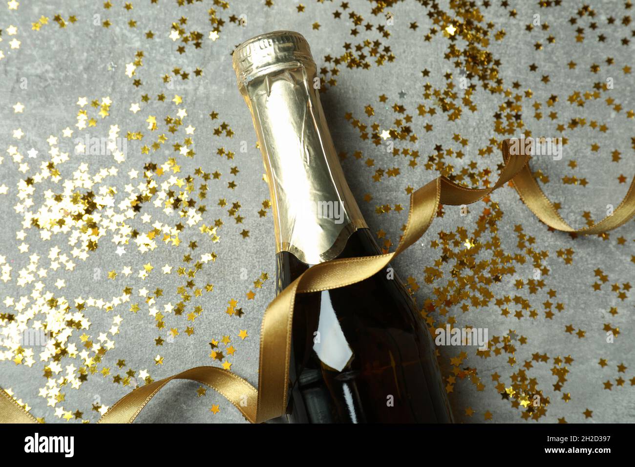 Bottle of champagne, glitter and ribbon on gray texture background ...