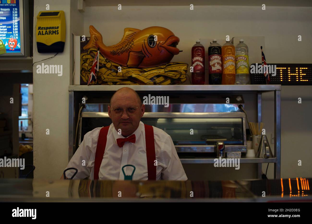 Fish and chip shop vendor wearing a red bow-tie and braces, fish and chip shop, Rugby, England Stock Photo