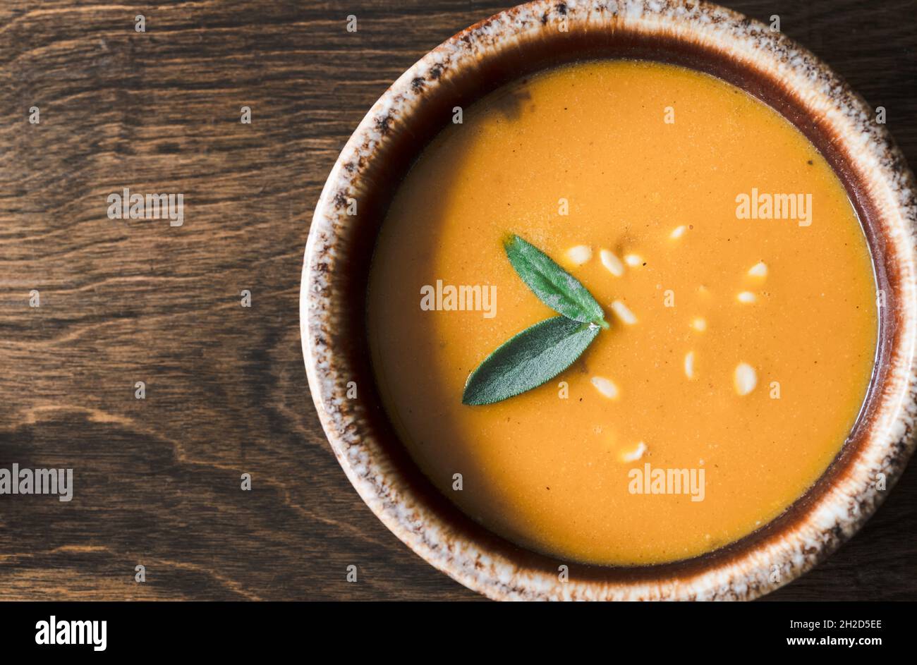 Squash Soup in Bowl on Wood Table with Sage and Nut Garnish Stock Photo