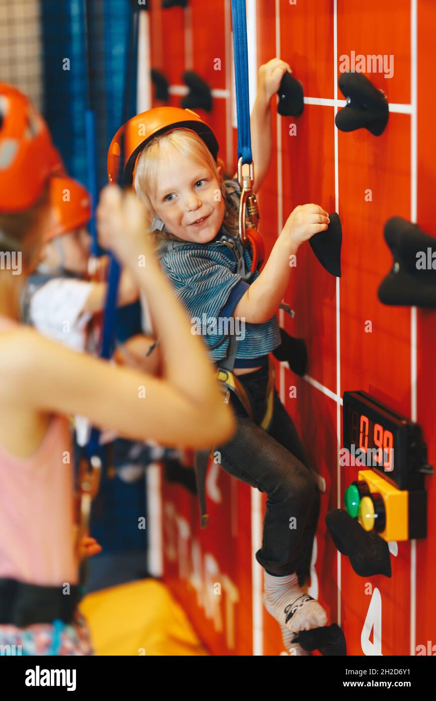 Indoor climbing activities for kids. Schoolboy smiling at the camera and having fun in an indoor playground for children. Happy kids in red helmets Stock Photo