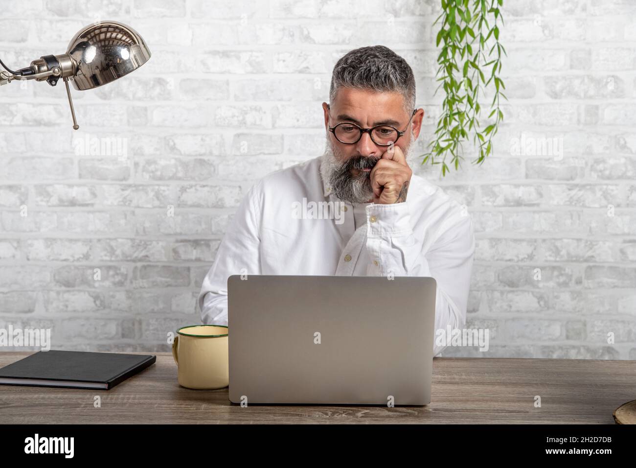 Serious and handsome freelancer sitting in front of computer with serious and thoughtful expression. Businessman thinks about solving some problems in Stock Photo
