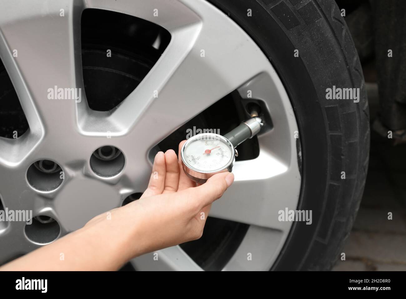 Woman checking car tire pressure with air gauge, closeup Stock Photo