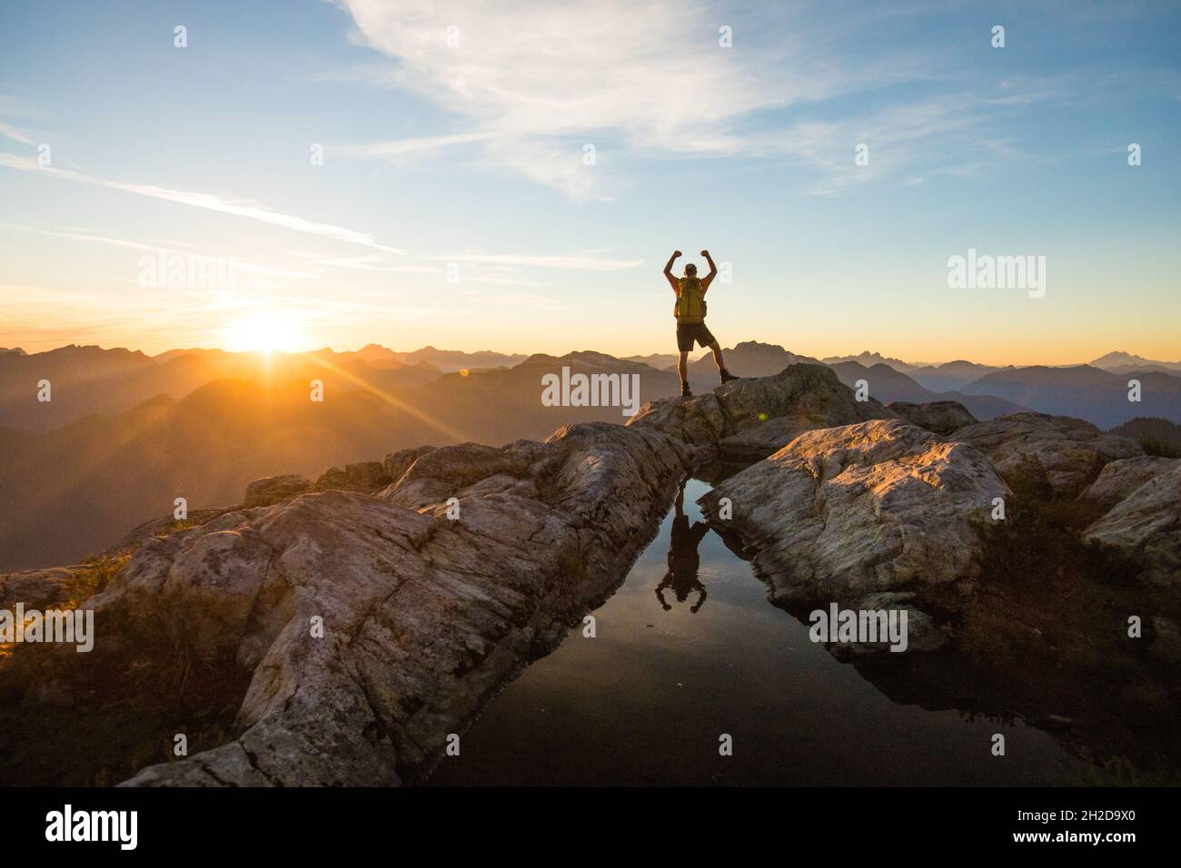 Successful hiker reaches mountain summit at sunset. Stock Photo