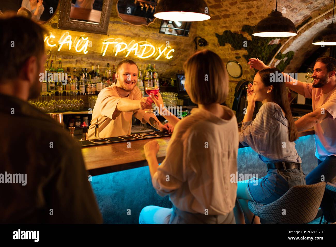 Barman giving alcohol drink to cheerful clients while working in pub