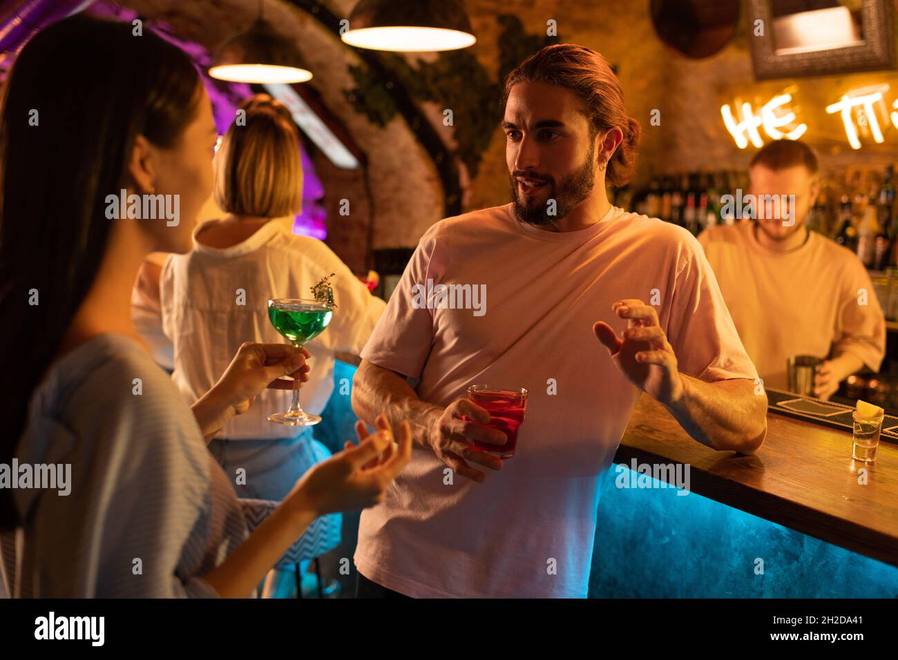 Bearded man with alcohol drink telling story to girlfriend near bar counter at night Stock Photo