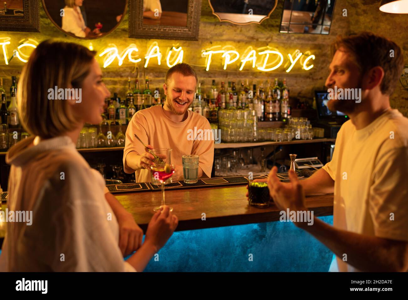 Happy barman serving alcohol drinks to talking couple during work in
