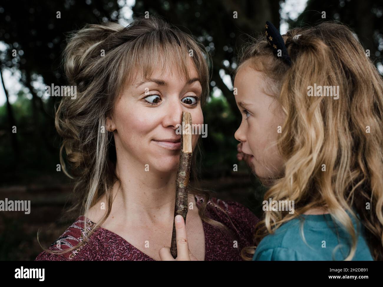 daughter playing funny faces with sticks with mother cross eyed Stock Photo