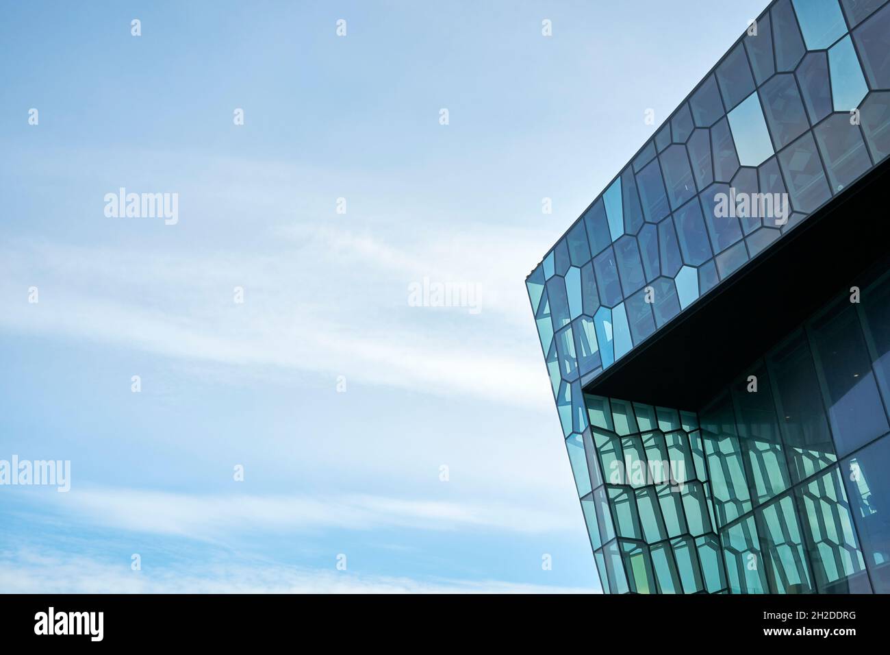 Low angle exterior corner of contemporary building with geometric shaped glass panels against cloudy blue sky in Reykjavik city in Iceland Stock Photo