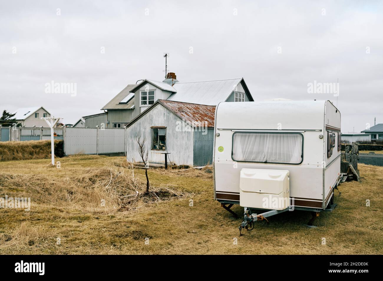 Camping trailer parked on lawn against houses and old barn under cloudy sky in fall season in Iceland Stock Photo