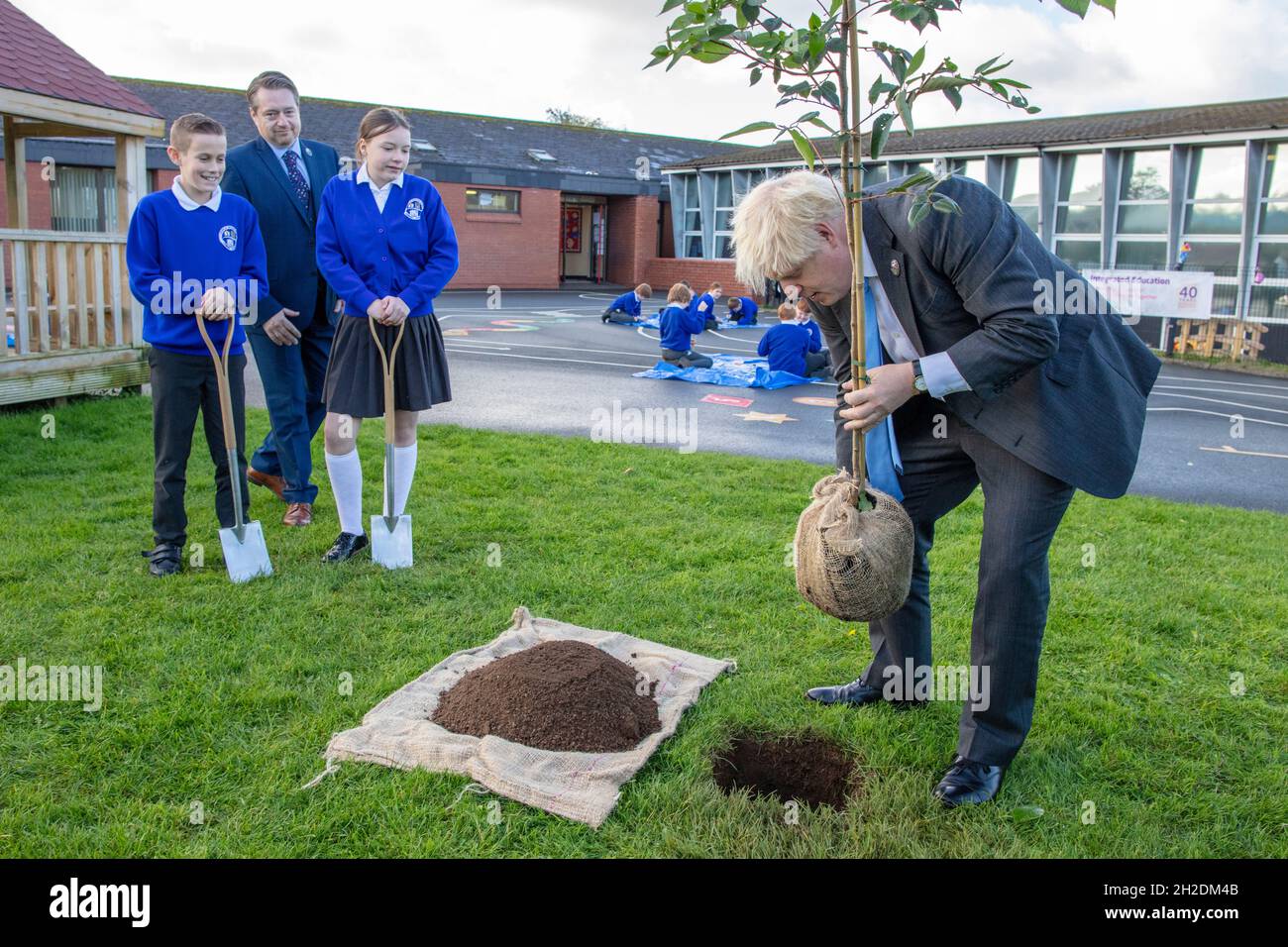 Prime Minister Boris Johnson plants a tree with help from P7 pupils Sophie and Oscar during a visit to Crumlin Intergrated primary school in County Antrim. Picture date: Thursday October 21, 2021. Stock Photo