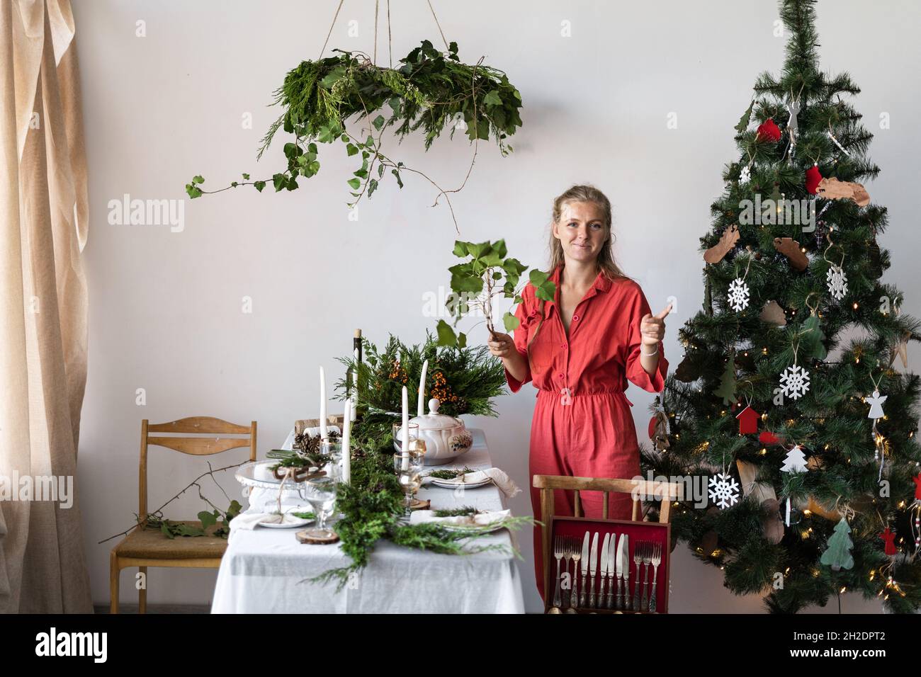 Living room decor with a festive table for Christmas. The girl decorates the room for the New Year. Decorated Christmas tree in the corner of the room Stock Photo