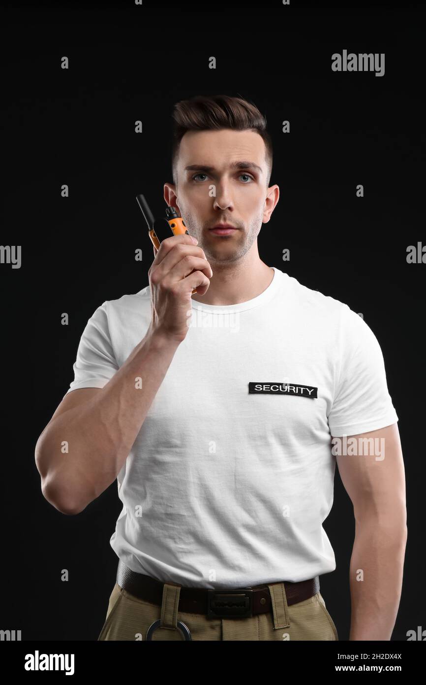 Male security guard using portable radio transmitter on dark background