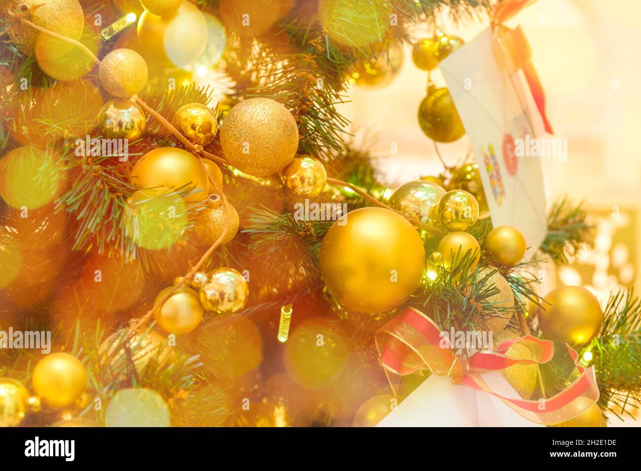 Christmas tree decorated with golden balls and envelope with letter to Santa Claus on a blurred and sparkling background  Stock Photo