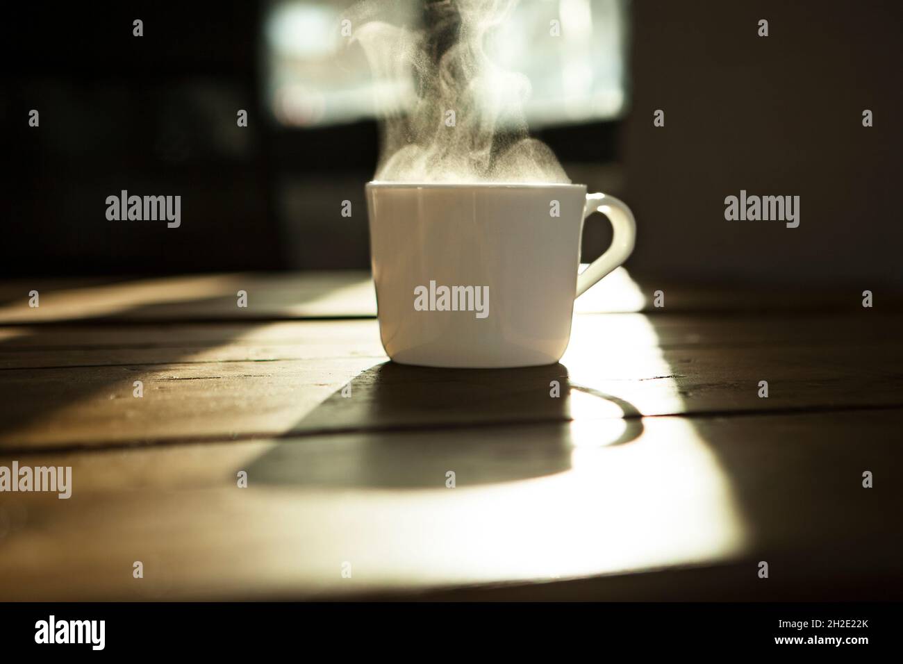 White coffee/tea Mug, white mug with hot beverage on wooden table, backlit. Stock Photo