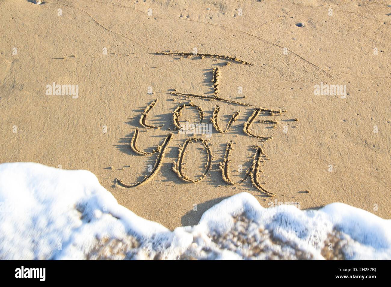 Words I Love You writing on the sand on beach against background. Love letters on the sand with sea foam. Stock Photo