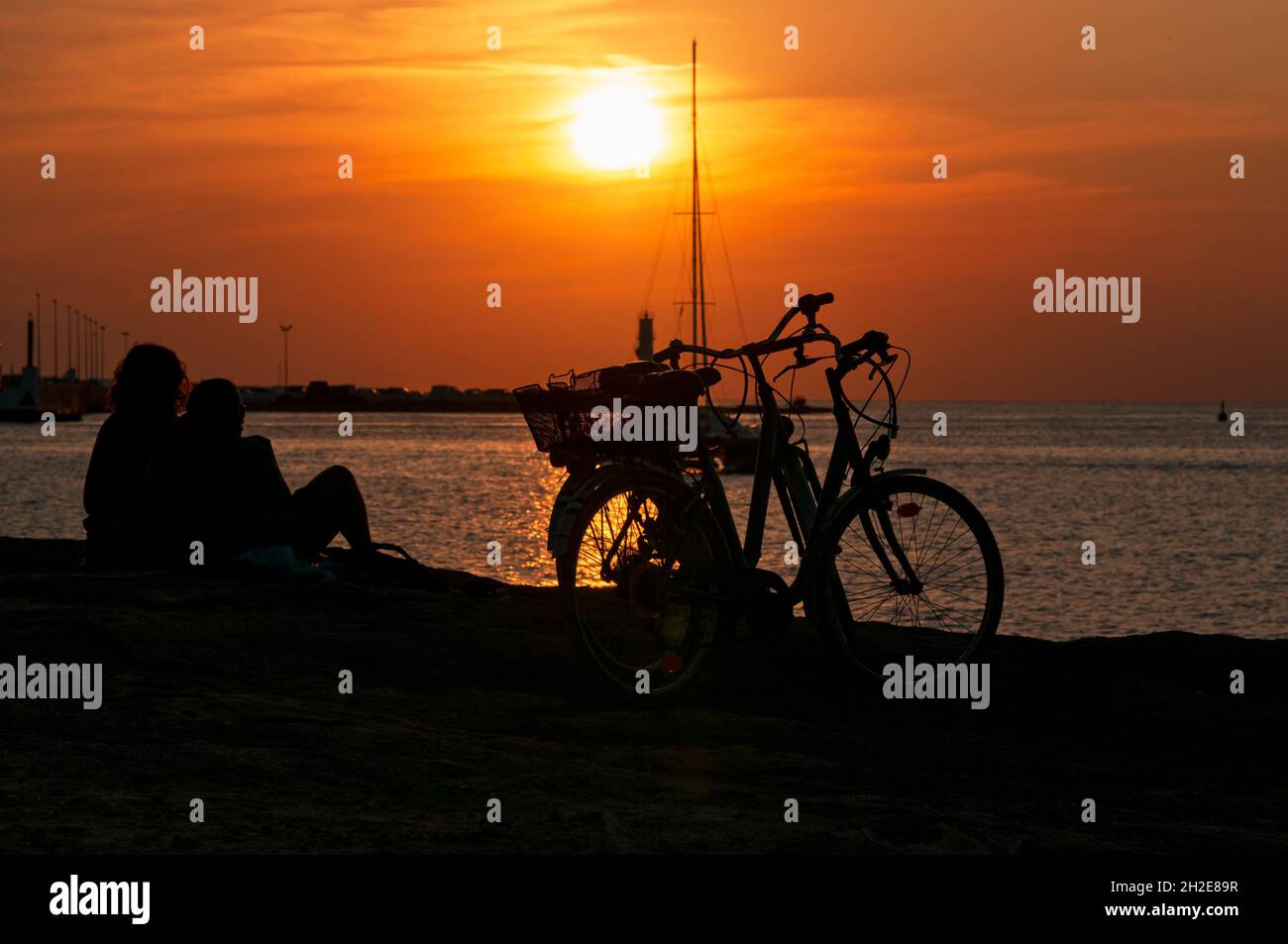 A couple in love watching the sunset over the sea next to their bicycles on the island of Formentera in Spain. Stock Photo