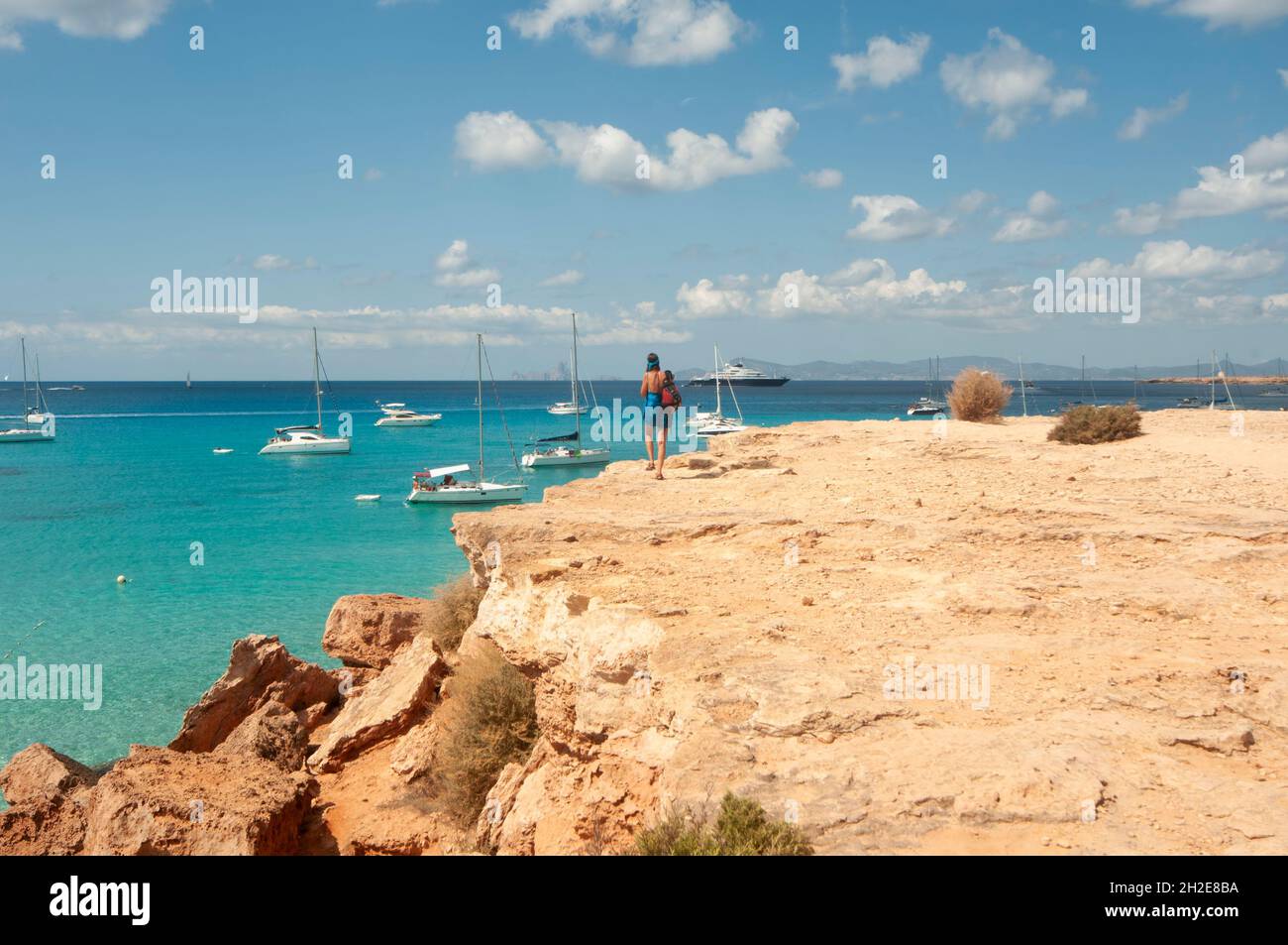 A young tourist looks at the horizon over the Mediterranean Sea from the edge of the rocky coastline, on the island of Formentera in Spain Stock Photo