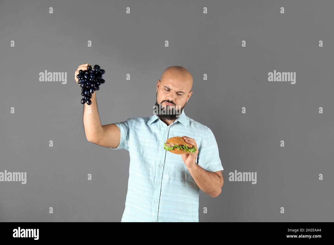 How Much Grapes Contribute To Obesity Reference: Overweight Man With Hamburger And Grapes On Gray Background Stock