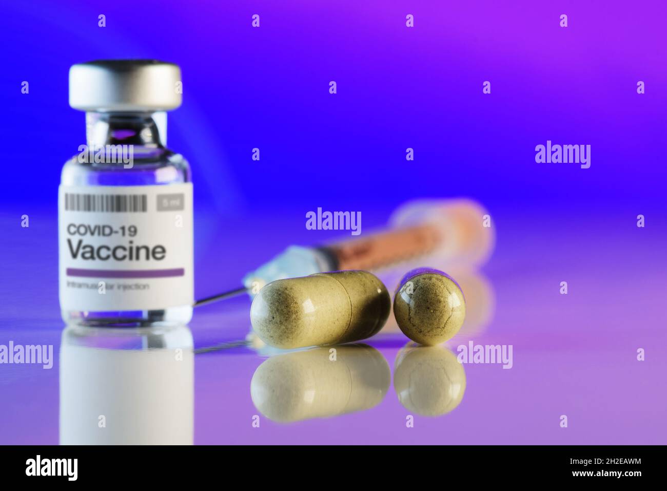 Close-up of two capsules with alternative medicine, COVID-19 vaccine vial and syringe in background. Alternative medicine, vaccination, Covid-19, phar Stock Photo