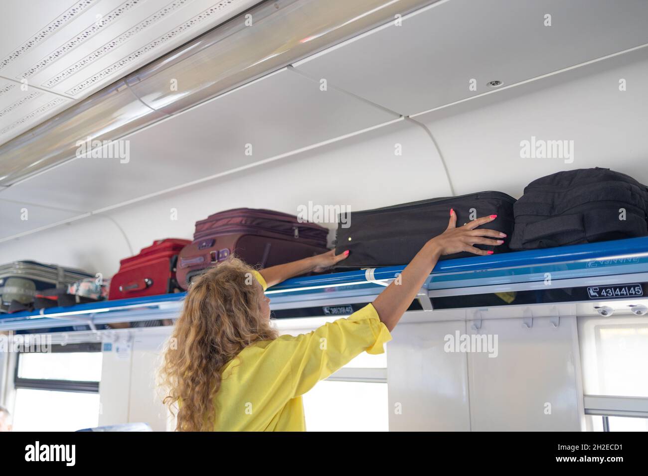 Businesswoman taking bag from luggage compartment in train. Holiday
