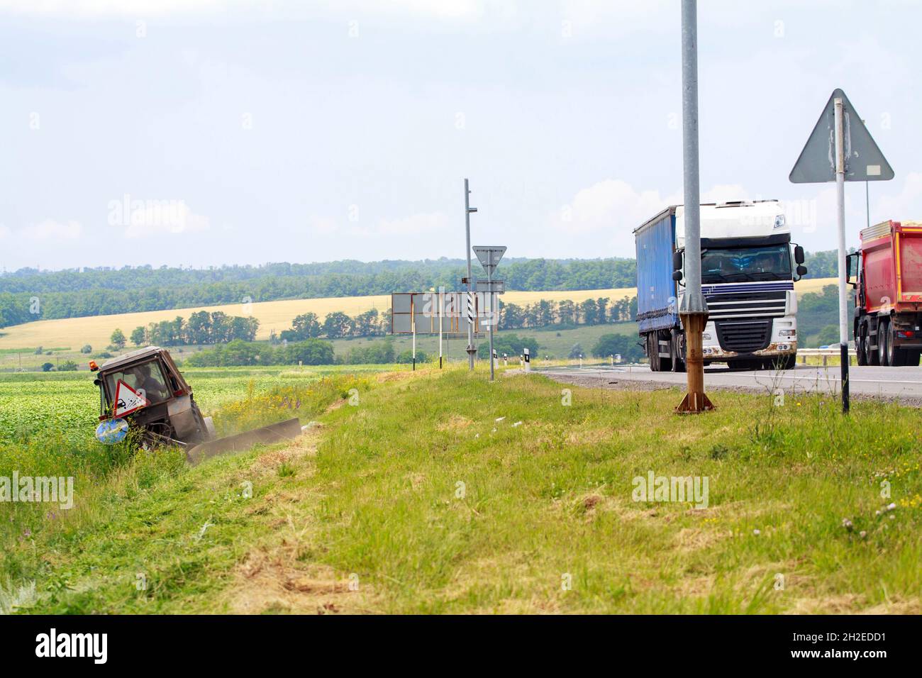 Tractor with a mechanical mower mowing grass on the side of the asphalt road Stock Photo