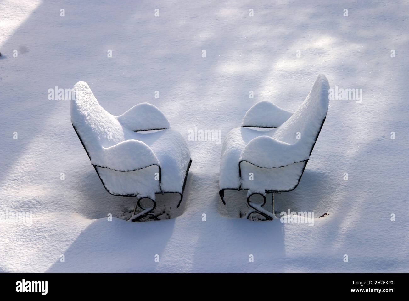 Two lonely deck chairs heavily covered in snow face each other companionably as they wait out the winter Stock Photo