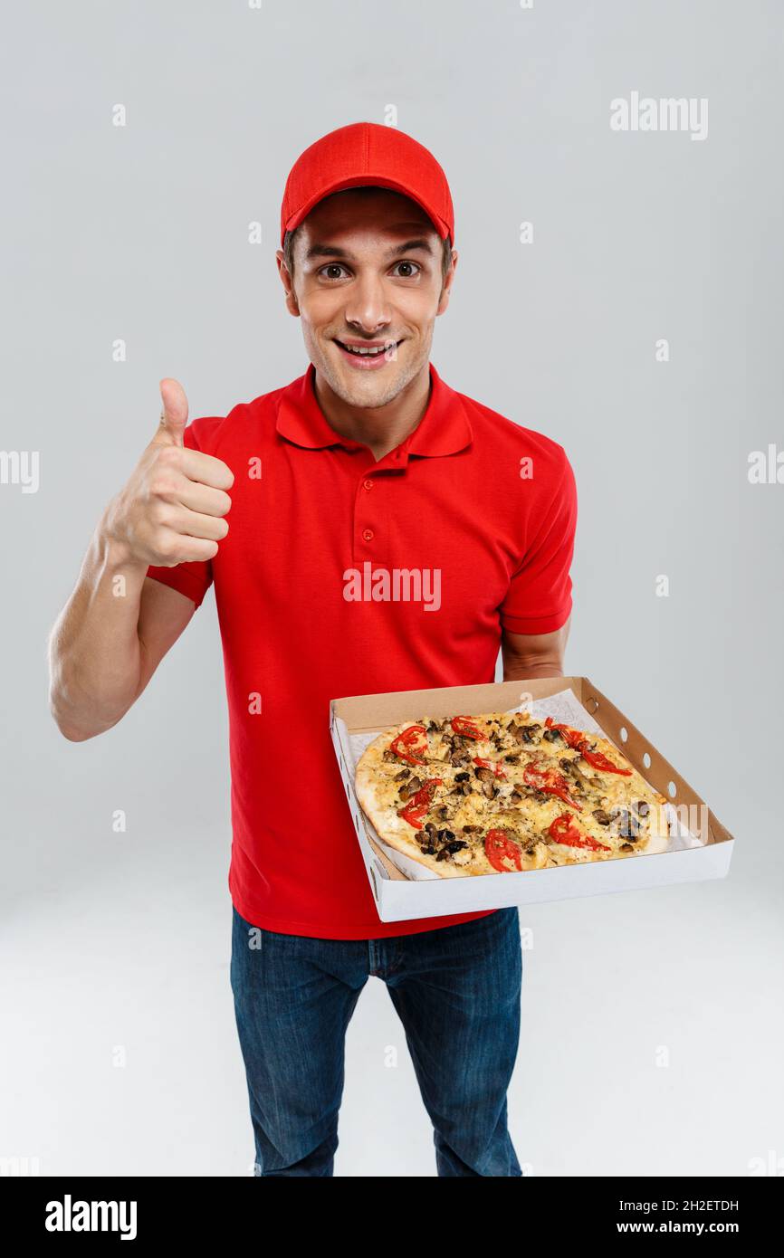 Young delivery man in uniform showing thumb up while showing pizza ...