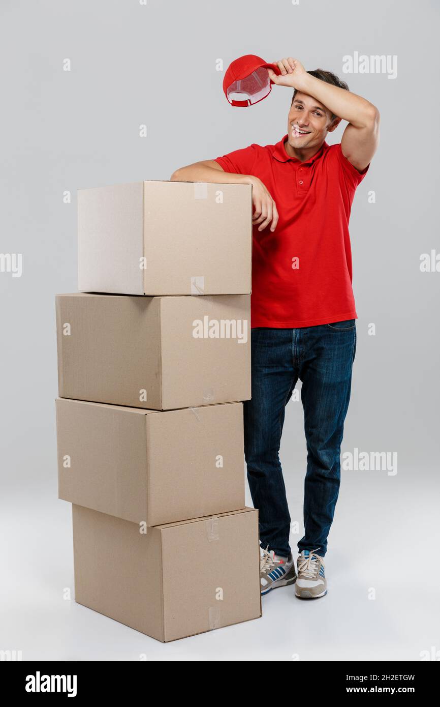 Young delivery man wiping his forehead while posing with cardboard ...