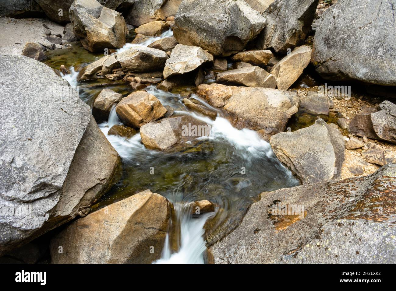Closeup of a narrow stream with long exposure surrounded by rocks in a ...
