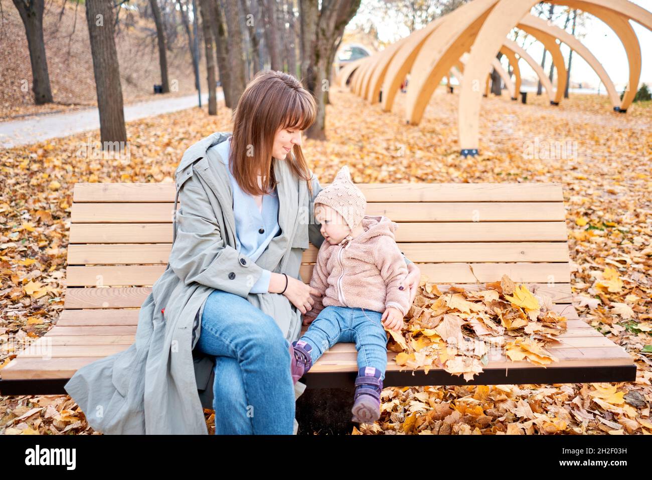 Portraits of a cute 1 year old baby girl and her young mother. Walking in Yellow Autumn Park. Leaf fall and yellow leaves. sunny day Stock Photo