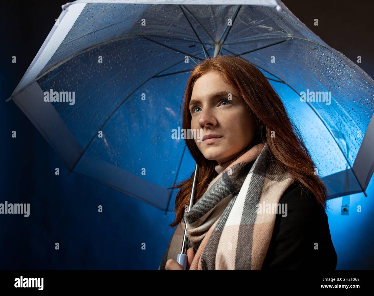 Portrait of beautiful red hair girl with blue eyes standing under transparent umbrella at night Stock Photo