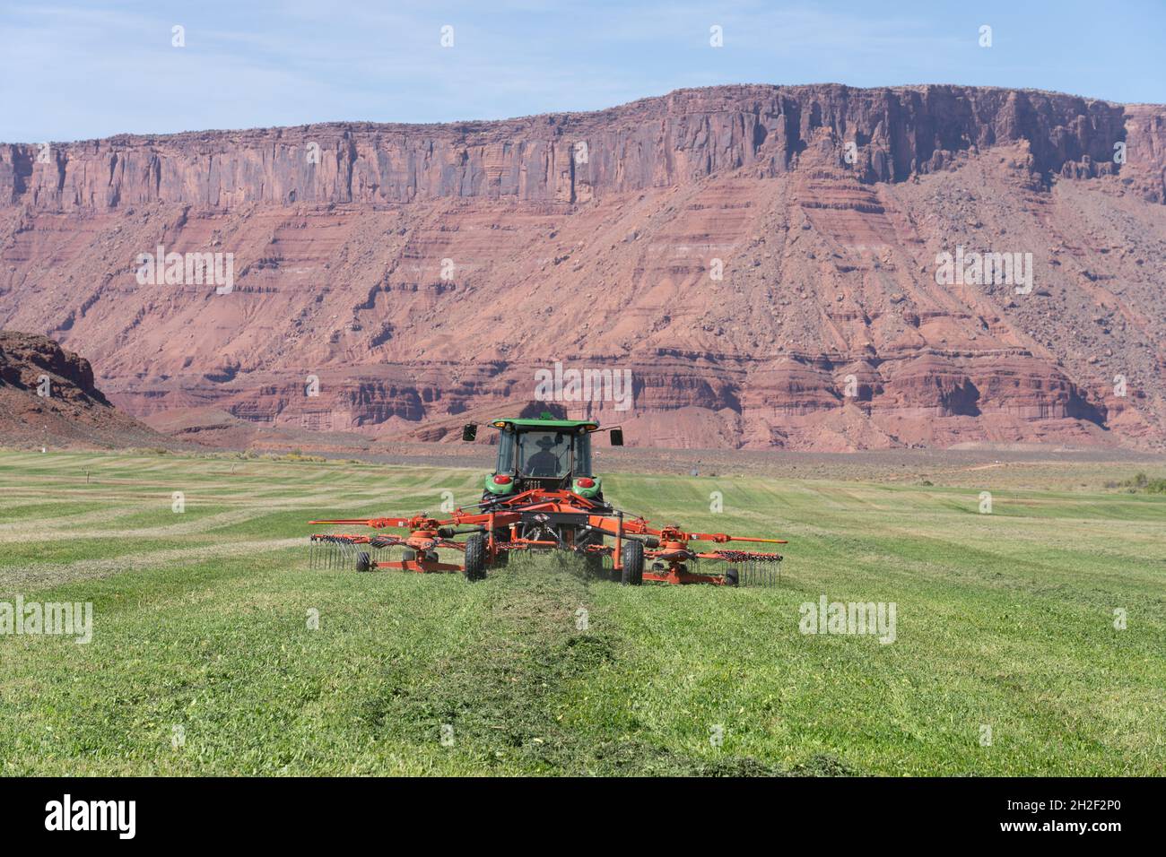 A rancher runs a rotary hay rake behind a tractor on a scenic ranch in ...