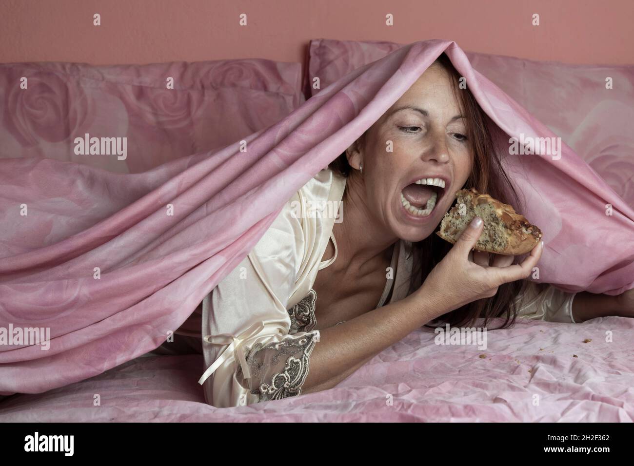 Night gluttony theme, woman on bed secretly eating a piece of pie Stock Photo