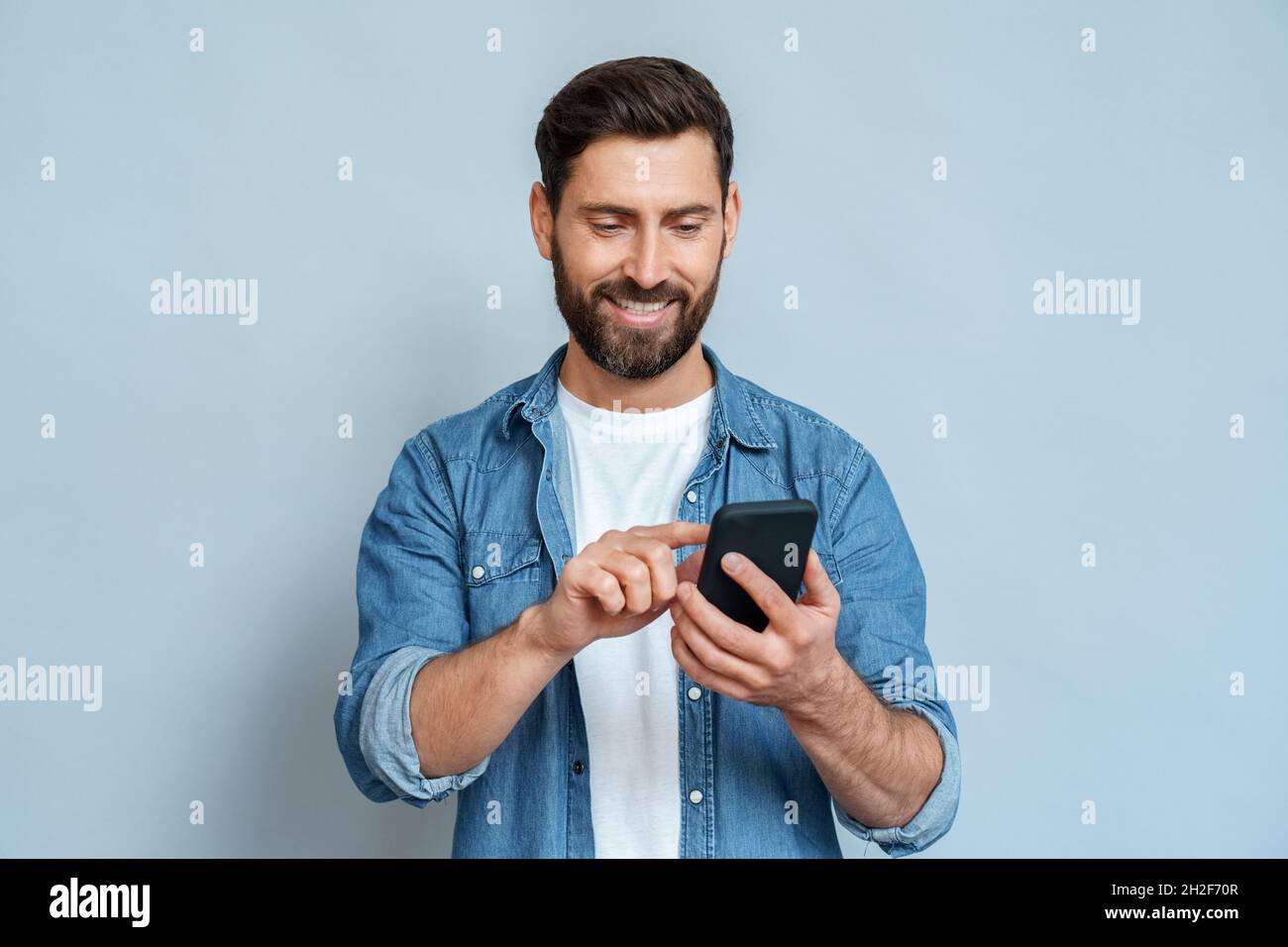 Smiling man using smartphone standing isolated on blue background copy space Stock Photo