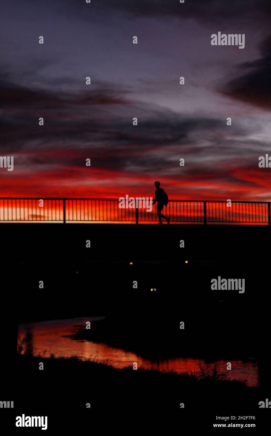Silhouette of a man walking along the bridge against orange sunset sky ...