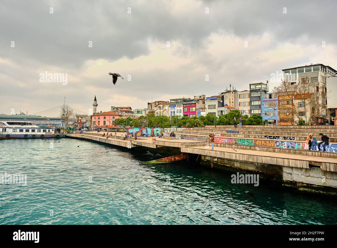 Karakoy shore and colorful painting on seating area and a man waiting for fishing with rod in istanbul golden horn and bosphorus and young couples Stock Photo