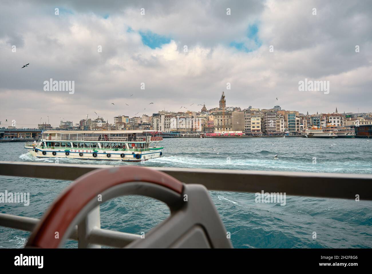 Galata tower golden horn in istanbul by taking photo from pedestrian ferry for internal transportation in istanbul during overcast weather and seagull Stock Photo