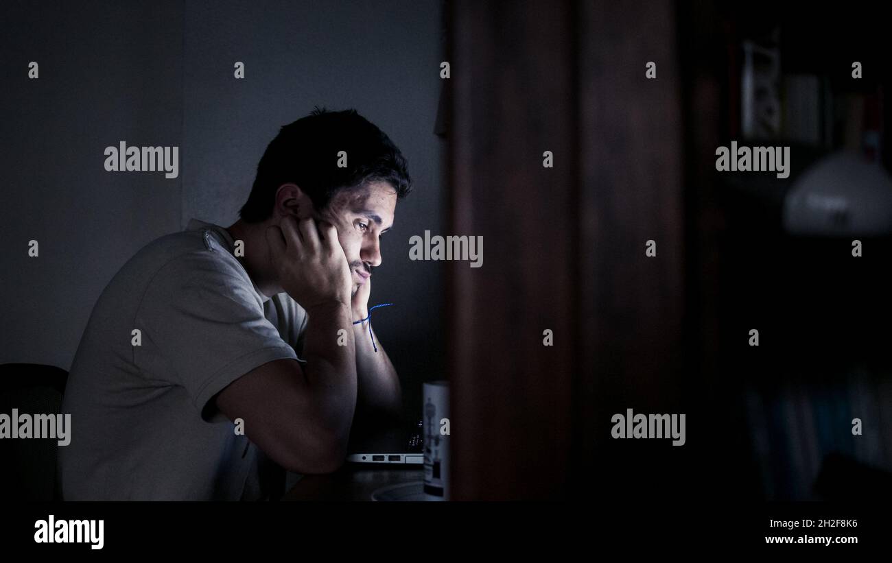 Hard-working man struggles to continue working on laptop at night Stock Photo