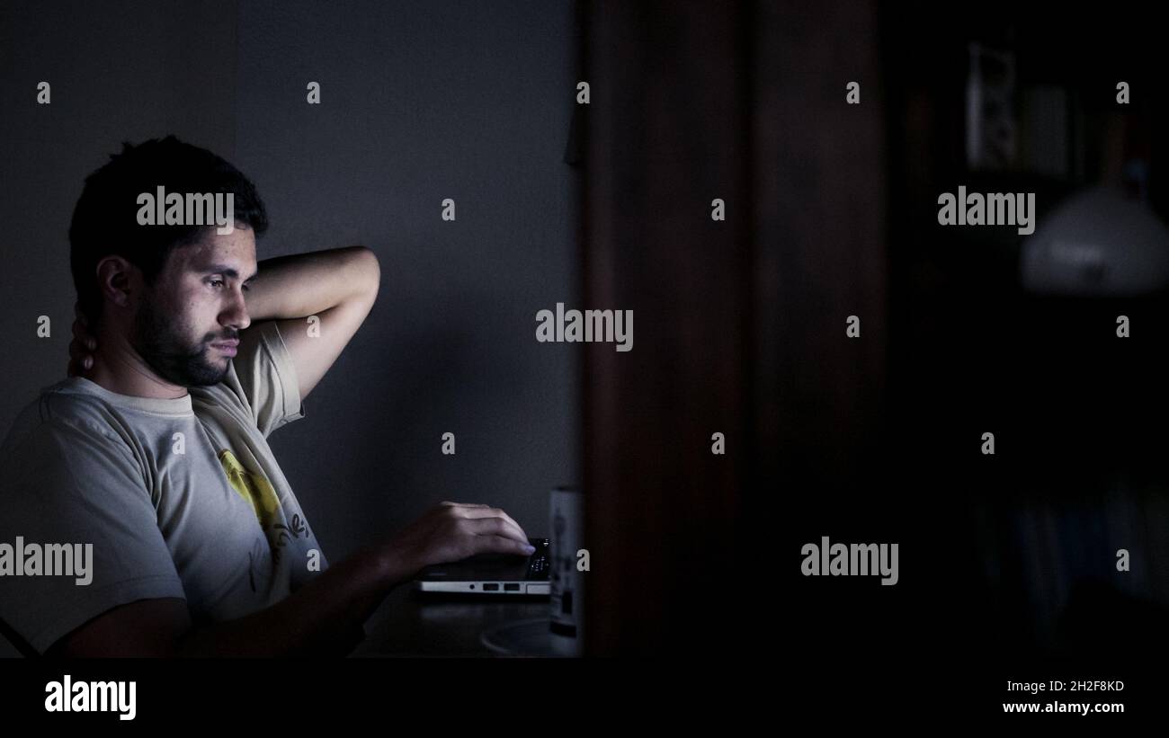 Hard-working man struggles to continue working on laptop at night Stock Photo