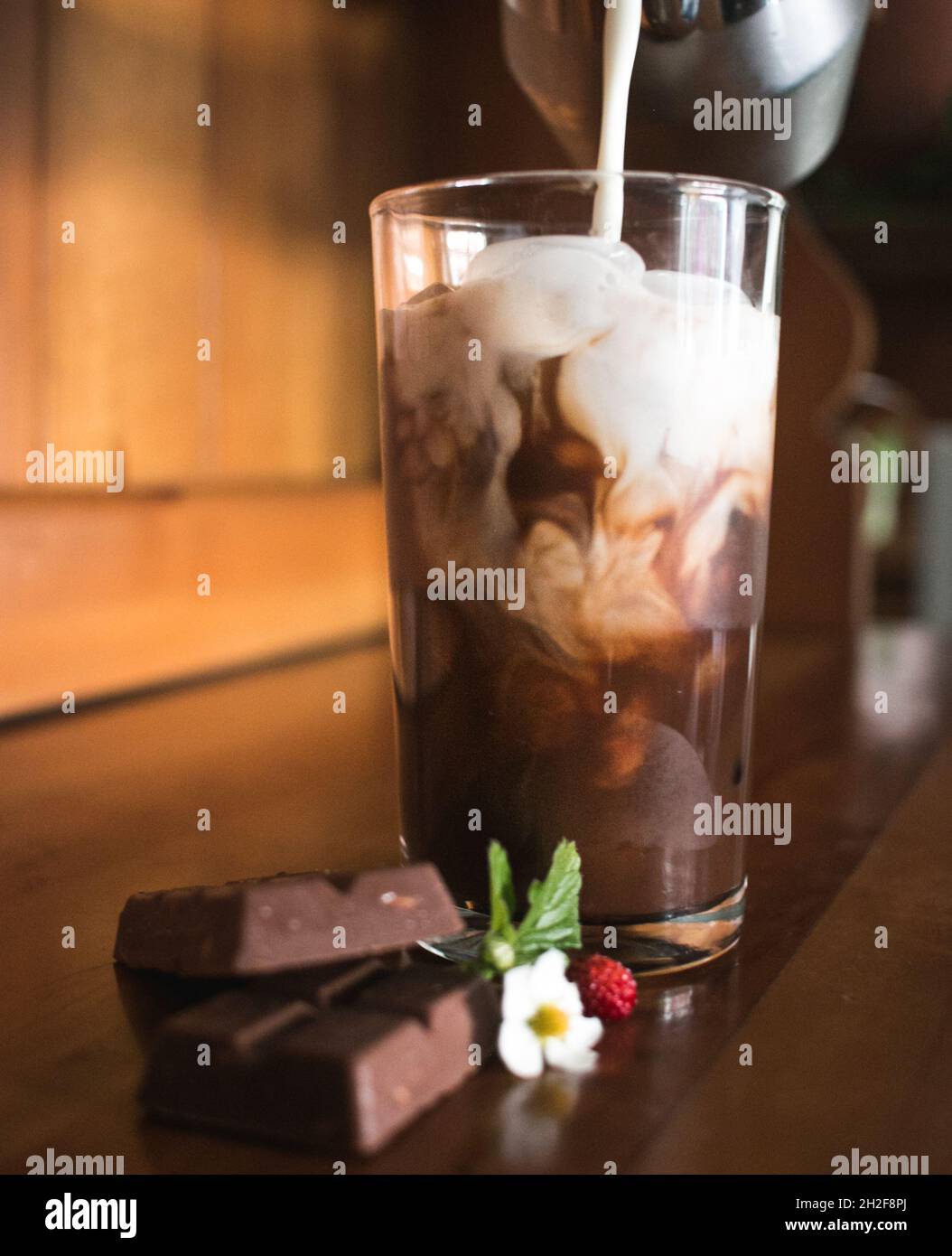 Delicious iced coffee on brown wooden table, decorated with leaves, chocolate and wild strawberries Stock Photo