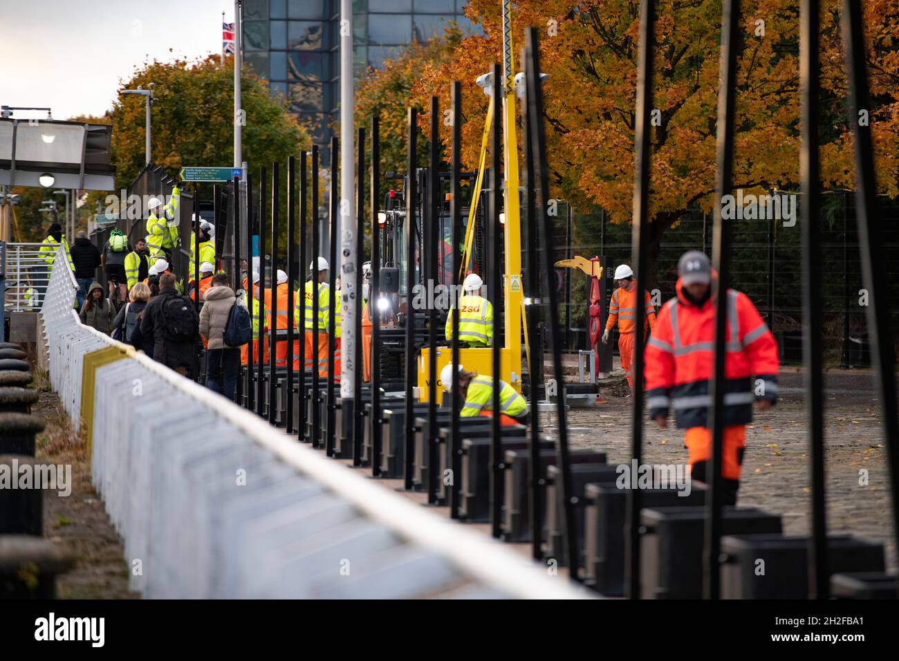 Glasgow, Scotland, UK. 21st Oct, 2021. PICTURED: Workmen wearing high viz PPE install part of the security perimeter fence to prevent any protestors gaining entry to the site. 10 days until the start of COP26. The COP26 site showing temporary structures half built on the grounds of the Scottish Event Campus (SEC) Previously known as Scottish Exhibition and Conference Centre (SECC). Security fences with a ‘ring of steel' encapsulates the COP26 conference site. CCTV stations with emergency lights and loudspeakers are positioned all over the site. Credit: Colin Fisher/Alamy Live News Stock Photo